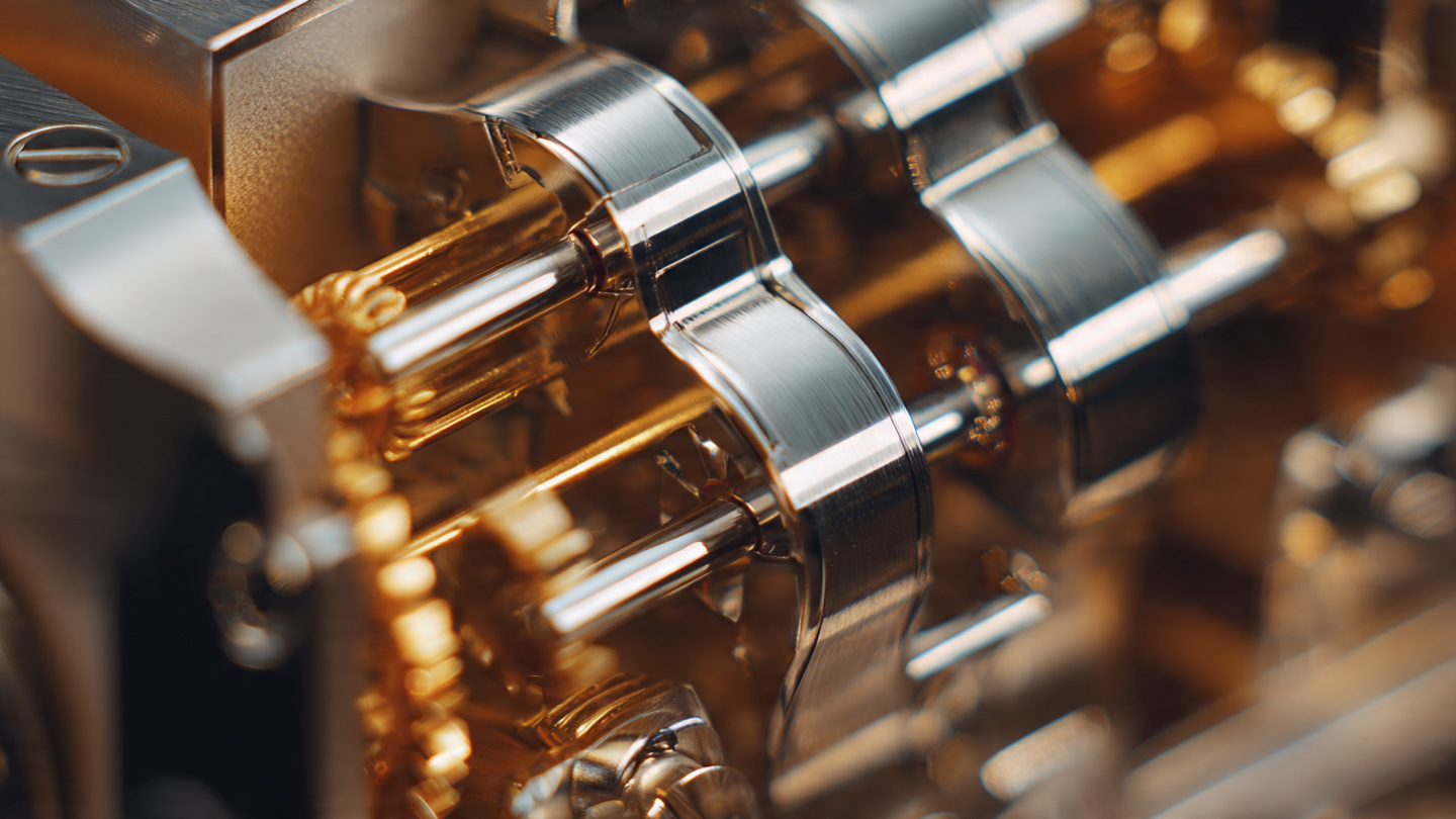 Macro photograph of a skeletonized watch movement showing four mainspring barrels arranged in series with polished steel bridges and a curved power reserve indicator under warm directional lighting