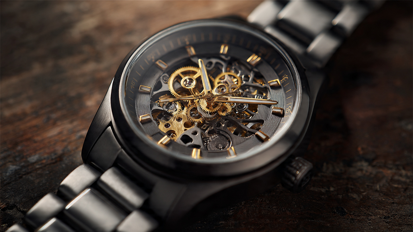 Macro photograph of a gray plasma ceramic skeleton watch with gold-toned movement gears under warm amber lighting